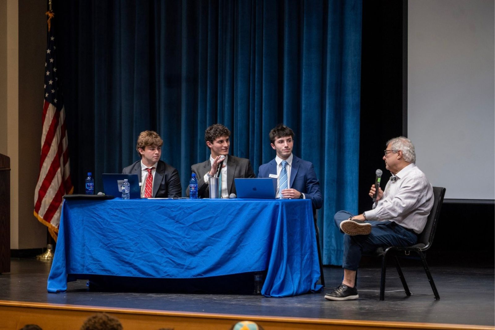 The student panel questioning Steve Koonin on the Riverwood stage, with the American flag at left